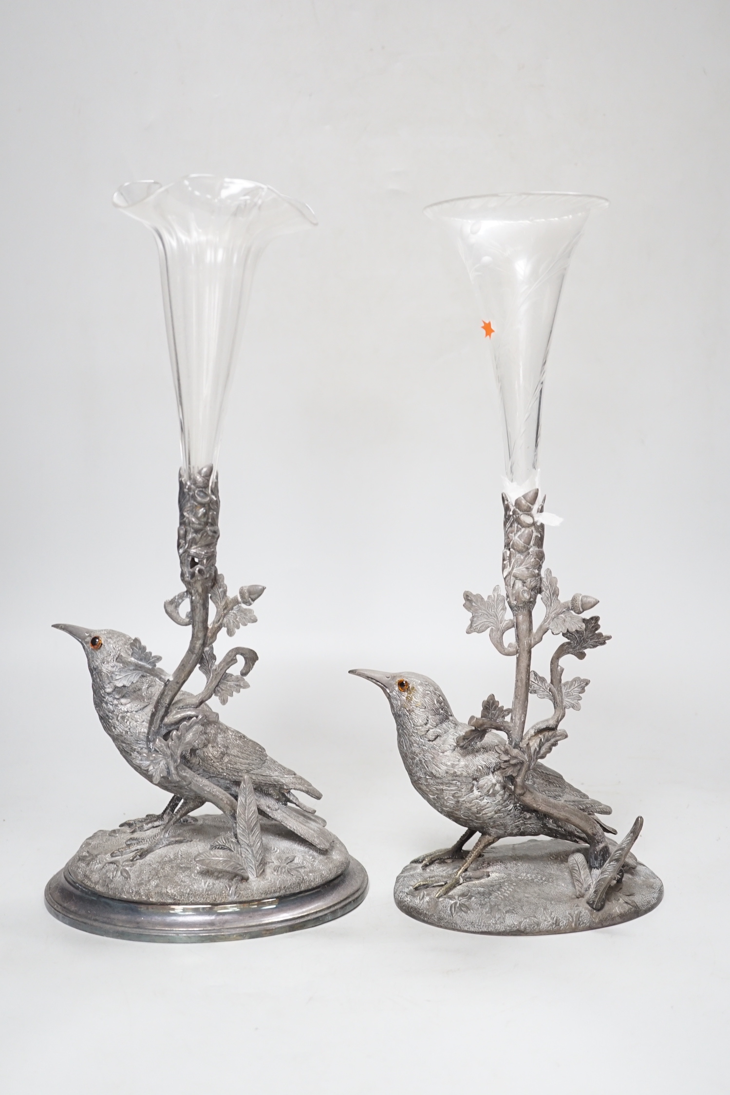 A matched pair of silver plated bird vases, with glass flutes, one with etched decoration, the largest 35cm high